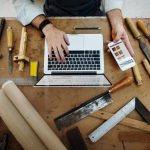 Un artisan concentré en tablier et chemise en jean utilise un niveau à bulle jaune pour vérifier la planéité d'un projet en bois dans son atelier