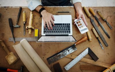 Un artisan concentré en tablier et chemise en jean utilise un niveau à bulle jaune pour vérifier la planéité d'un projet en bois dans son atelier