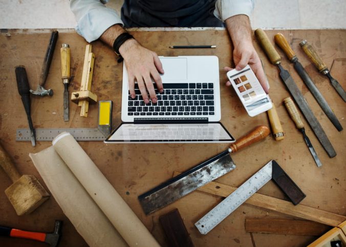 Un artisan concentré en tablier et chemise en jean utilise un niveau à bulle jaune pour vérifier la planéité d'un projet en bois dans son atelier