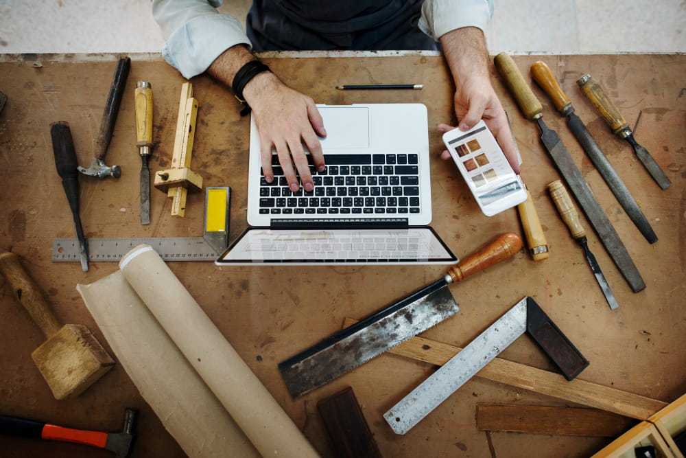 Un artisan concentré en tablier et chemise en jean utilise un niveau à bulle jaune pour vérifier la planéité d'un projet en bois dans son atelier